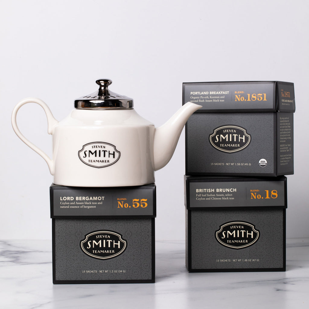Three cartons of black tea with a white porcelain teapot.