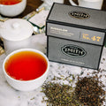 Black box of Bungalow tea with Smith logo next to a brewed cup of tea and loose blend.