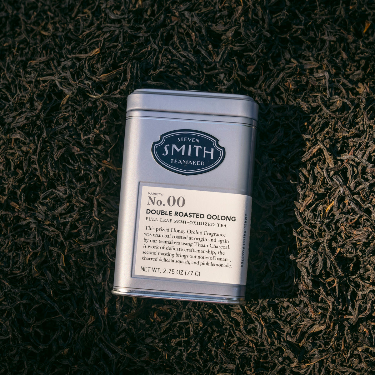 Grey tin of Double Roasted Oolong tea laying on a bed of loose leaf oolong tea.